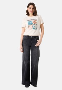Camiseta gráfica beige con diseños en azul y marrón, combinada con jeans de pierna ancha negros de denim. Detalles simples de botones y bolsillos.