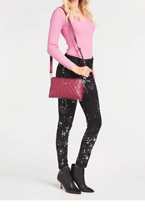 Bolso acolchado burdeos con herrajes plateados, combinado con vaqueros negros salpicados y una camiseta de manga larga rosa con canalé, llevado con botas negras hasta el tobillo.
