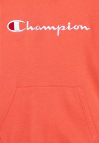 Sudadera de felpa coral con el logo "Champion" en bordado blanco. Incluye un bolsillo delantero y puños acanalados. Textura suave y diseño casual.