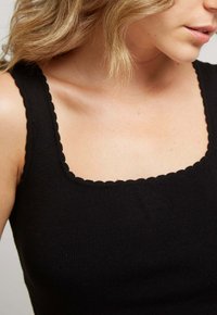 Débardeur noir à côtes avec un col carré aux bords festonnés. Le tissu semble doux et ajusté.