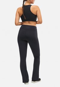 Sujetador deportivo negro y leggings negros acampanados hechos de un tejido elástico. La cinturilla es ancha y plana, con un mínimo de marca en la parte posterior.