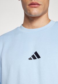 Lyseblå sweatshirt med rund halsudskæring, prydet med et sort Adidas-logo i grafisk stil på brystet og en blød bomuldsstruktur.