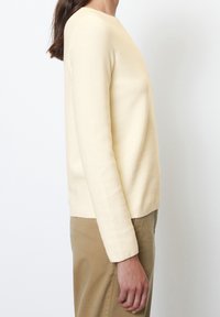 Pull crème texturé avec un col rond simple et des manches longues, présentant une coupe décontractée et un ourlet droit, associé à un pantalon kaki.