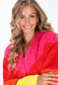 Manteau en fausse fourrure coloré avec des sections rose, rouge et jaune. Texture douce, design en V et col proéminent. Manches longues.