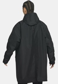 Cappotto impermeabile nero con cappuccio, caratterizzato da maniche lunghe e una vestibilità comoda, realizzato in materiale liscio e opaco. La vista posteriore mostra un taglio dritto.