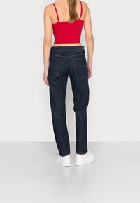 Mörkblå denimjeans med rak passform, bakfickor med böjd söm, kombinerat med vita sneakers och en röd linne.