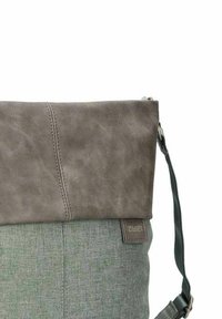 Zaino in tessuto grigio e verde e pelle con cuciture visibili e spallacci regolabili su sfondo bianco.