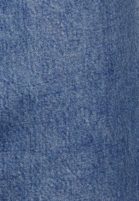 Denimstof i mellemblå farve med en tekstureret vævning. Har lette variationer og en subtil glans, der er karakteristisk for bomuldsdenim.