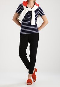 Top de rayas en azul marino y blanco de manga corta con un diseño de estrella, combinado con pantalones negros y tacones rojos de punta abierta, acentuado con un suéter blanco.