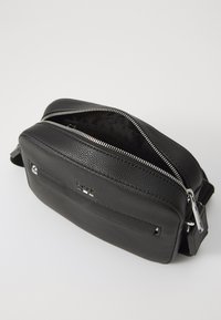 Black leather crossbody bag with textured surface, dual zippered compartments, and silver-tone hardware. Features a front pocket.