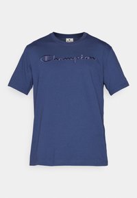 Modré bavlněné tričko s krátkým rukávem a kulatým výstřihem; na přední straně má vyšívané logo "Champion" v tmavě fialové barvě.