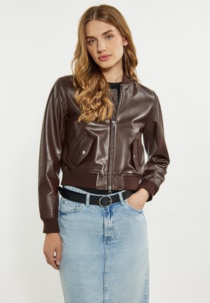 Giacca bomber in finta pelle marrone con chiusura zip, polsini a coste, due tasche frontali e design cropped, abbinata a una gonna di denim blu chiaro.