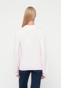 Gaisni rozā adīta džemperis ar garām puffed piedurknēm, ribotām aprocēm un apakšmalu. Vienkāršs apaļš apkakles izgriezums bez redzamām rakstainēm vai akcentiem.