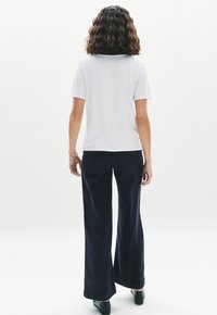 Top blanco de manga corta y pantalones anchos en color navy, con una textura suave. El atuendo se completa con zapatos negros, fotografiado desde atrás.