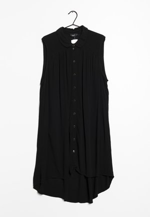 Robe noire sans manches à boutons avec plis et col arrondi suspendue sur un cintre noir sur fond blanc.