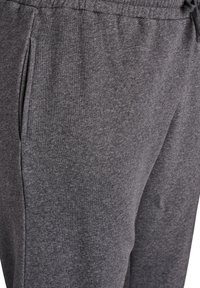Pantalones de chándal grises hechos de un tejido suave, con cinturilla con cordón, bolsillos laterales y un ajuste casual con una textura lisa.