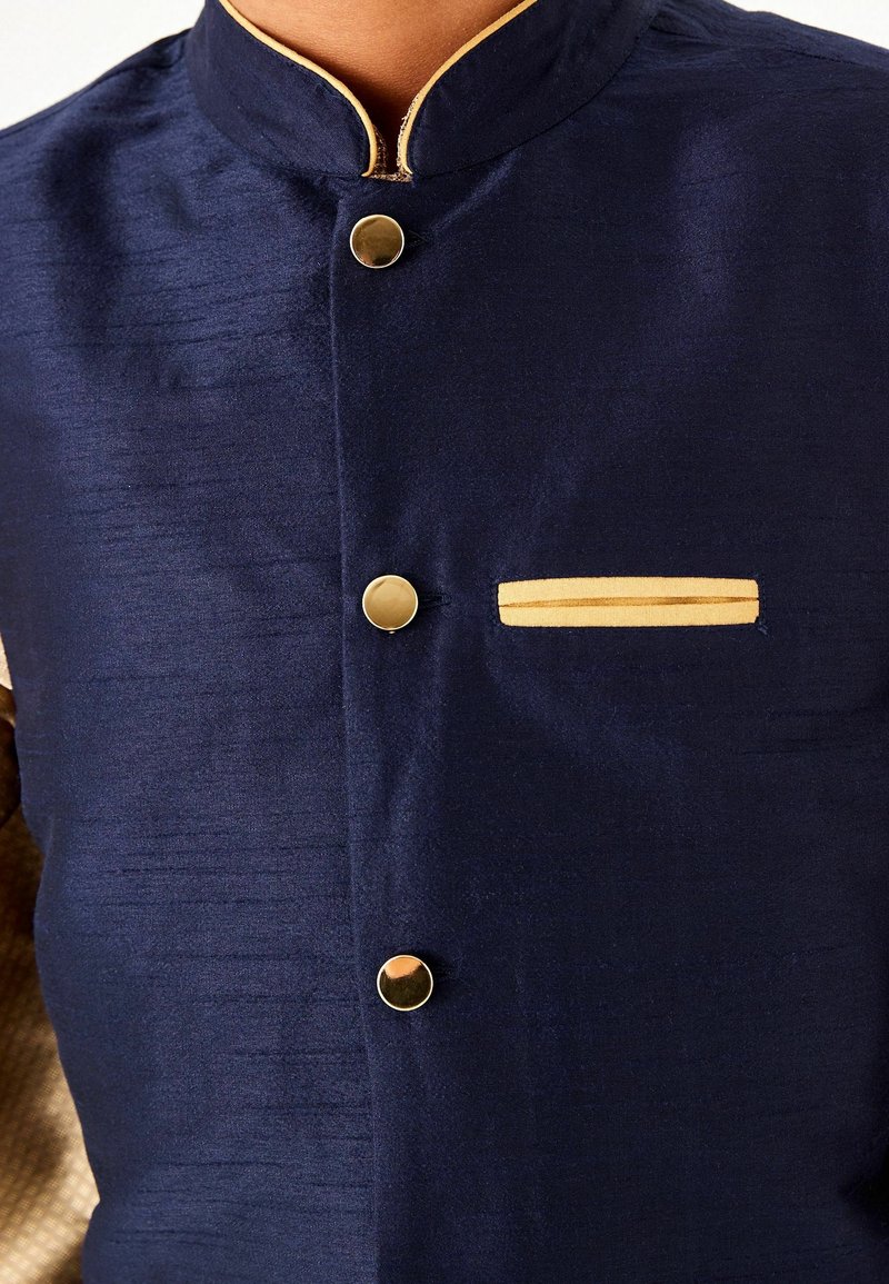 Gros plan sur une veste traditionnelle bleu marine avec des boutons dorés, un col mandarin et une poche poitrine bordée d’or.