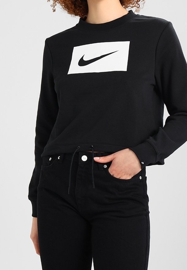 Sweat-shirt noir court avec col ras du cou, arborant un logo rectangulaire blanc à l'avant. Association avec un jean noir, présentant un détail de cordon de serrage.