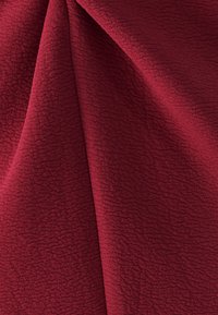 Teksturowana, głęboka czerwona tkanina z subtelnym, wypukłym wzorem; miękka i giętka o lekko puszystej powierzchni. Geometryczny wzór zwiększa wizualną głębię.