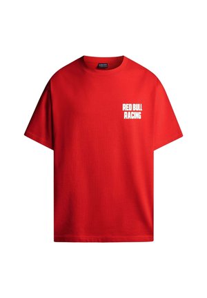 Homme aux cheveux bouclés portant un t-shirt rouge avec un texte blanc sur Madrid, la course et les tapas, main dans la poche arrière, de dos.