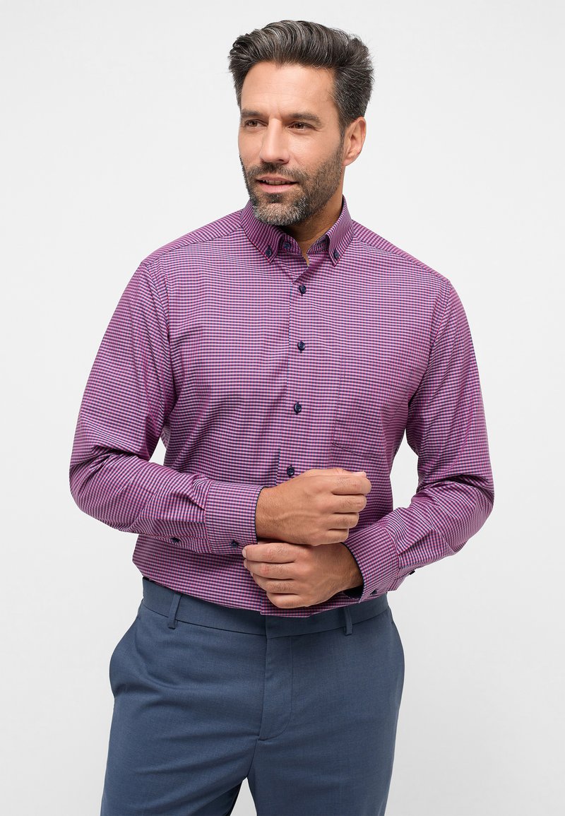 Camicia a quadri in cotone viola e bianco, con colletto a punta e bottoni scuri. Abbinata a pantaloni azzurri chiari.