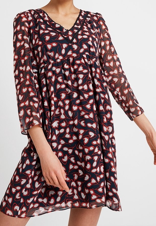 Valkoinen sydänkuvioinen, läpikuultava tummansininen mekko, jossa on V-pääntie, kolme neljäsosapituista hihaa ja kootut vyötärö. Yksityiskohtainen pääntien viimeistely.