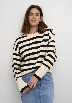 Cream and black striped sweater with a ribbed hem, wide cuffs, and three buttons on the shoulder. Paired with a light blue denim skirt.