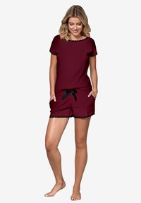 Burgundowy zestaw piżamowy z krótkimi rękawami, koronkowym wykończeniem i regulowanym pasem, składający się z szortów z falbaniastymi krawędziami. Miękki materiał.