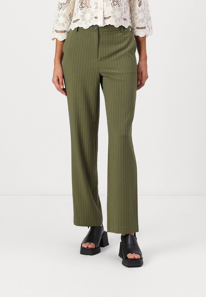 Olivengrønne bukser med striber og straight-leg design. Stoffet ser glat ud. Kombineret med sorte åbne hæle med blok.