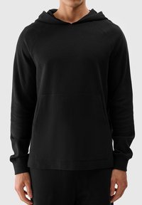 Schwarzer Kapuzenpullover mit geripptem Struktur, vorderer Kängurutasche und langen Ärmeln. Hat eine lockere Passform und ein minimales Design.
