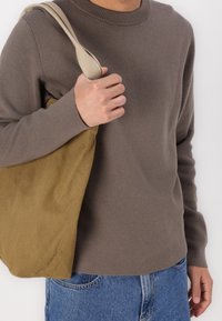Brauner Strickpullover mit rundem Halsausschnitt, kombiniert mit einer beigefarbenen Canvas-Tasche. Der Look wird mit blauen Jeans abgerundet.