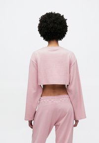 Rövidített rózsaszín pulóver hosszú ujjakkal, puha anyagból készült. Kerek nyakú és laza fazonú, hozzáillő nadrággal párosítva.