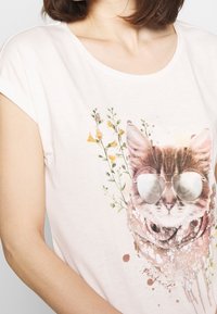 Camiseta de manga corta de color rosa claro con un gráfico de un gato con gafas de sol, adornada con ilustraciones florales y la palabra "Perfecto."
