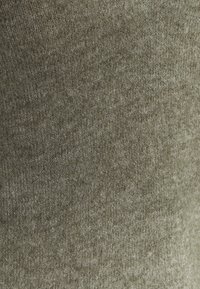 Tissu tricoté vert olive atténué avec une texture douce ; présente de légères variations de teinte, créant un aspect subtil et stratifié.