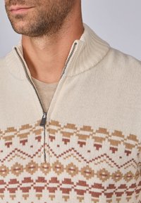 Pull en tricot crème avec un col montant et une fermeture éclair. Présente un motif géométrique aux ton chaud près de l'ourlet. Texture douce.