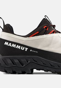 Χαμηλού κόψιμου πεζοπορικό παπούτσι Mammut σε μπεζ και μαύρο, με ύφασμα Gore-Tex και ανθεκτική σόλα με βαθιά εμπρόσθια αυλάκια, διακοσμημένο με κόκκινες λεπτομέρειες στα κορδόνια και θηλιά στο τακούνι.