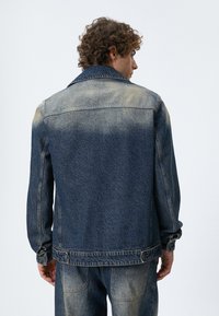 Mørkeblå denimjakke med afblegede områder, klassisk krave, knapmanchetter og to sidelommer, med en lige pasform.