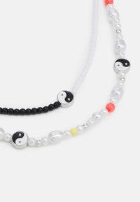 Colar de contas em preto e branco com pendentes de yin-yang, alternando entre contas de pérola e contas coloridas, com acentos em prata e detalhes texturizados.