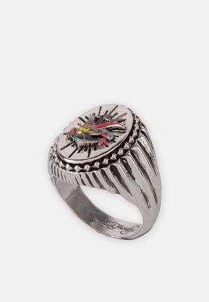 Silver ring with an oval face featuring a colorful bird design. Textured band with vertical grooves and raised accents around the face.