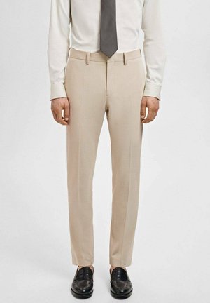 Beige skræddersyede dressbukser med en slank pasform, der har forlommer, glat front, bæltestropper og pressefolder; parret med sorte loafers.