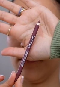 Konturówka do ust Isadora w kolorze ciemnego burgunda, z zwężanym końcem, z nadrukowanym na korpusie białym logo, trzymana w dłoni.
