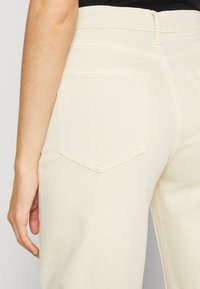 Beige jeans med rak ben, med en bakficka i diamantform och subtila sömdetaljer. Slät textur, hög midja.