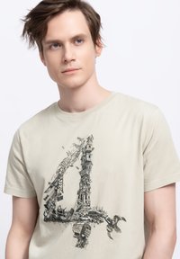 Beige katoenen T-shirt met een gedetailleerde afdruk van het cijfer "4" samengesteld uit verschillende bouwelementen en puin.