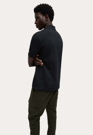 Zwart poloshirt met korte mouwen, katoenen materiaal, rechte snit, gedragen met olijfgroene cargobroek, gezien van achteren.