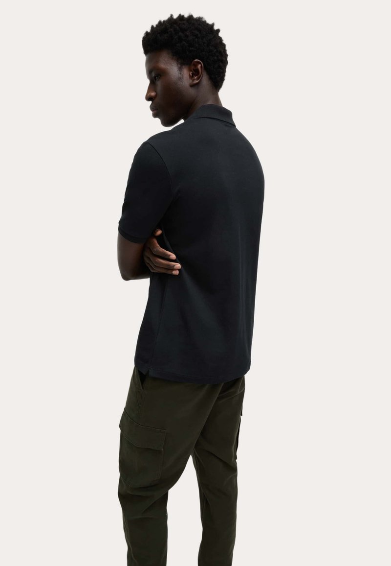 Sort poloshirt med korte ærmer, bomuldsmateriale, lige snit, båret med olivengrønne cargobukser, set bagfra.
