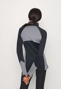 Long-sleeve athletic top featuring a two-tone design with dark gray and light gray sections, a zip neck, and extended cuffs for comfort.