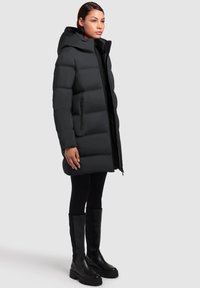 Black puffer coat with a hood, featuring a quilted design, front zipper, and side pockets. Paired with black leggings and knee-high boots.