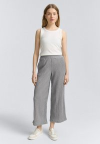 Pantalones anchos de pierna amplia en gris, con pliegues y de tejido ligero. Combinados con una blusa sin mangas blanca y zapatillas beige. Diseño simple y casual.