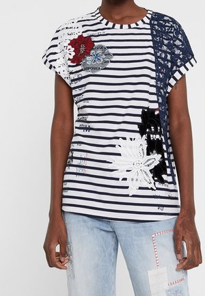 Raidallinen lyhythihainen t-paita, jossa on kukkakirjonta ja pitsiyksityiskohtia. Paita on pyöreäkauluksinen ja rento malli, valmistettu kevyestä kankaasta.