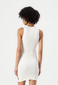 Valge ribakoonustatud kleit, millel on keha lähedane siluett, ilma varrukateta disain ja kontrastsed mustad aktsendid külgedel. Siledat tekstuuri.